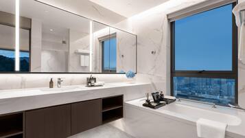A modern bathroom with a large mirror, a bathtub, and a city view through a large window.