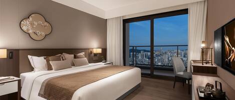 Una habitación de hotel moderna con una cama grande, vistas a la ciudad, un televisor de pantalla plana y un escritorio con lámpara.