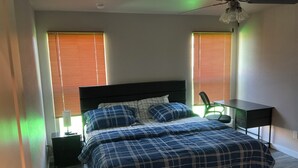 Un dormitorio con cama, escritorio y dos ventanas con persianas.