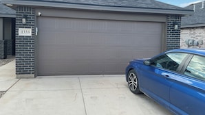 Un garaje residencial con una puerta gris, un coche azul estacionado al frente y el número 1333.