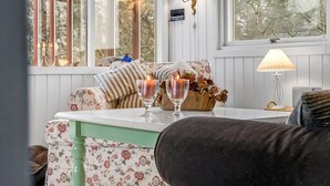 Een gezellige zithoek met een bank en een tafel, beide versierd met bloemmotieven. Twee kaarsen staan op tafel, en een lamp is zichtbaar aan de muur.