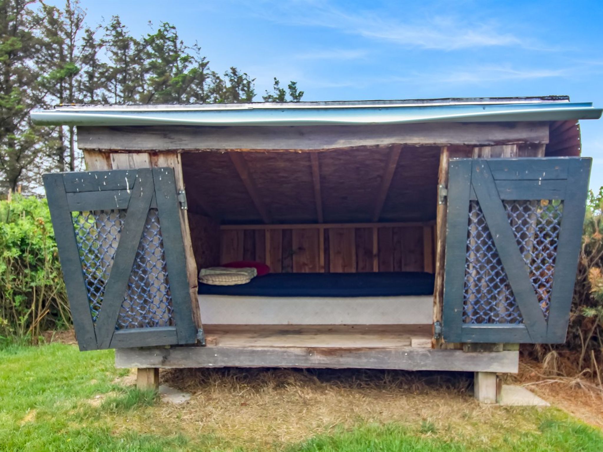 Een rustieke houten hut met een bed, openslaande houten deuren en een rieten dak.