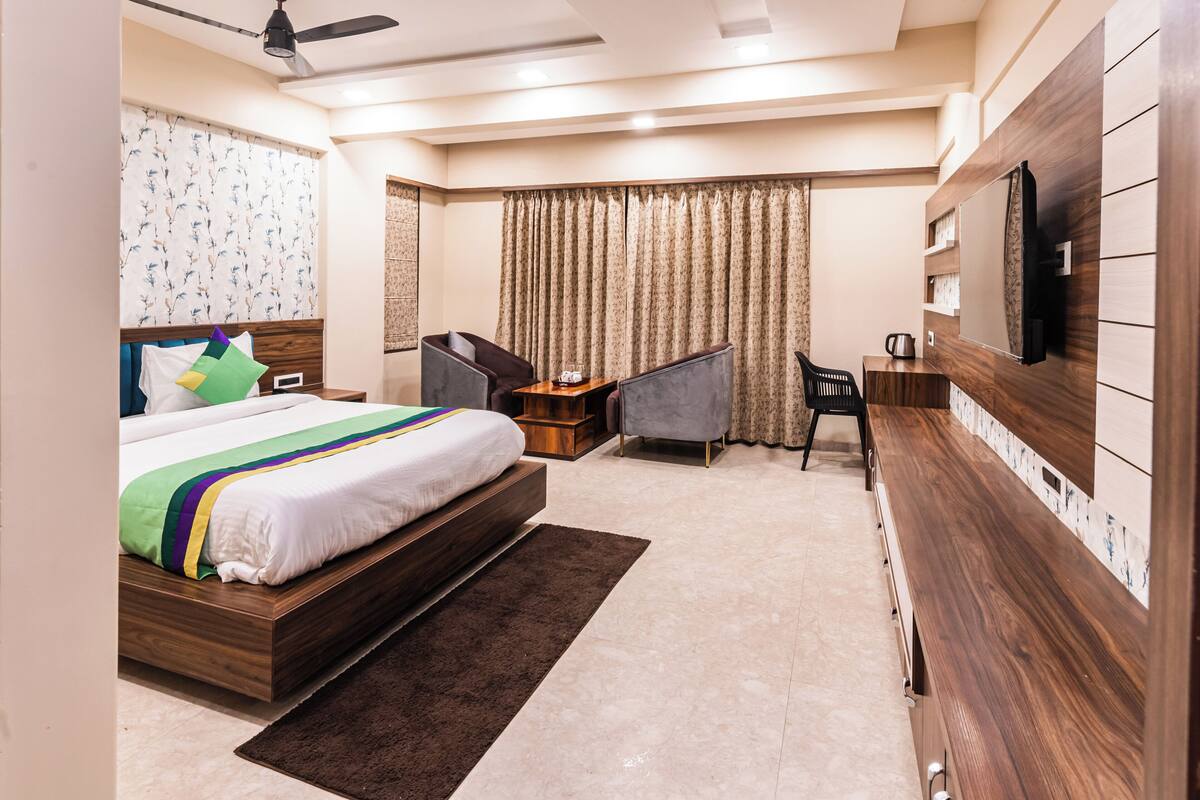 A modern hotel room with a large bed, a desk, a chair, a TV mounted on the wall, and a ceiling fan.