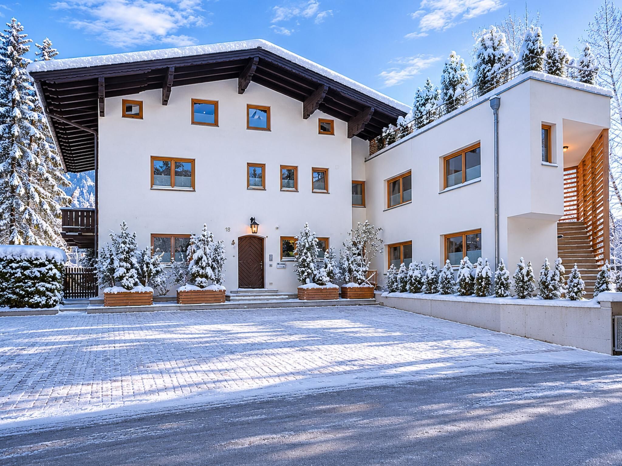 A modern two-story building with a snow-covered entrance, wooden balconies, and a paved driveway.