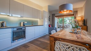 Una cocina moderna con armarios blancos, horno integrado y una zona de comedor con mesa y sillas de madera.