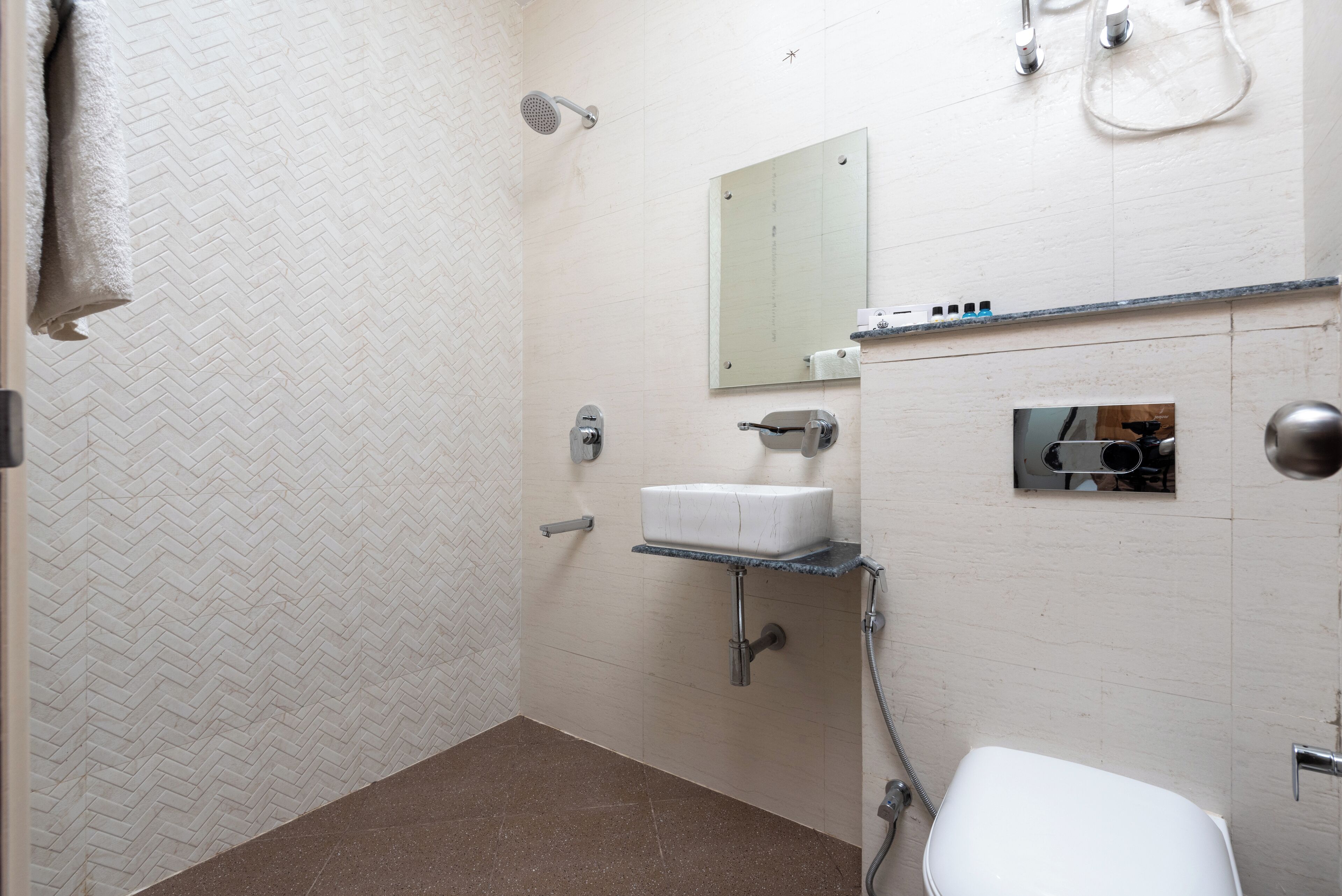A bathroom with a white herringbone-patterned wall, a white sink, a mirror, a shower, and a toilet.