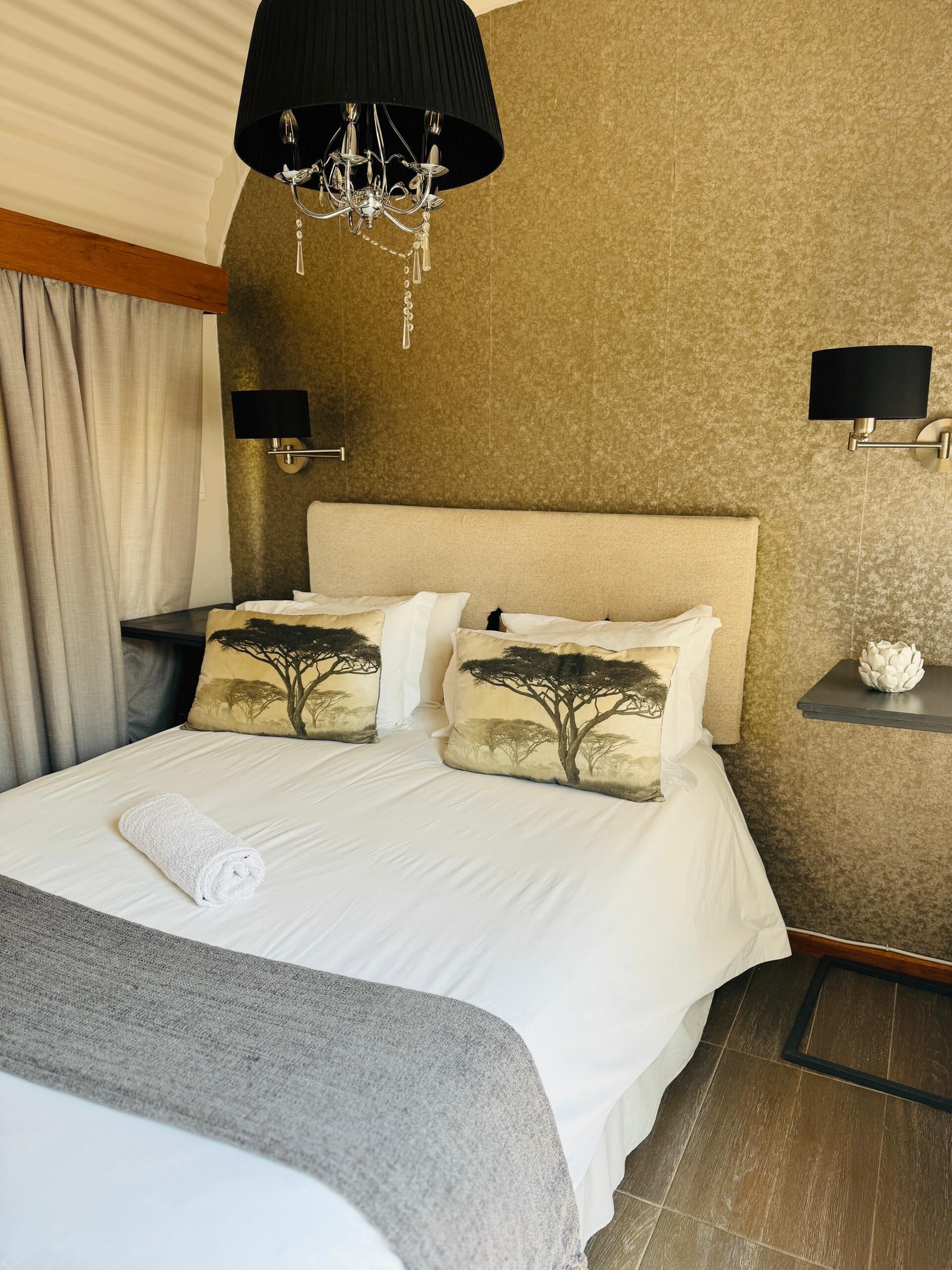 Een hotelkamer met een groot bed, twee wandlampen, een kroonluchter en een decoratief kunstwerk aan de muur.