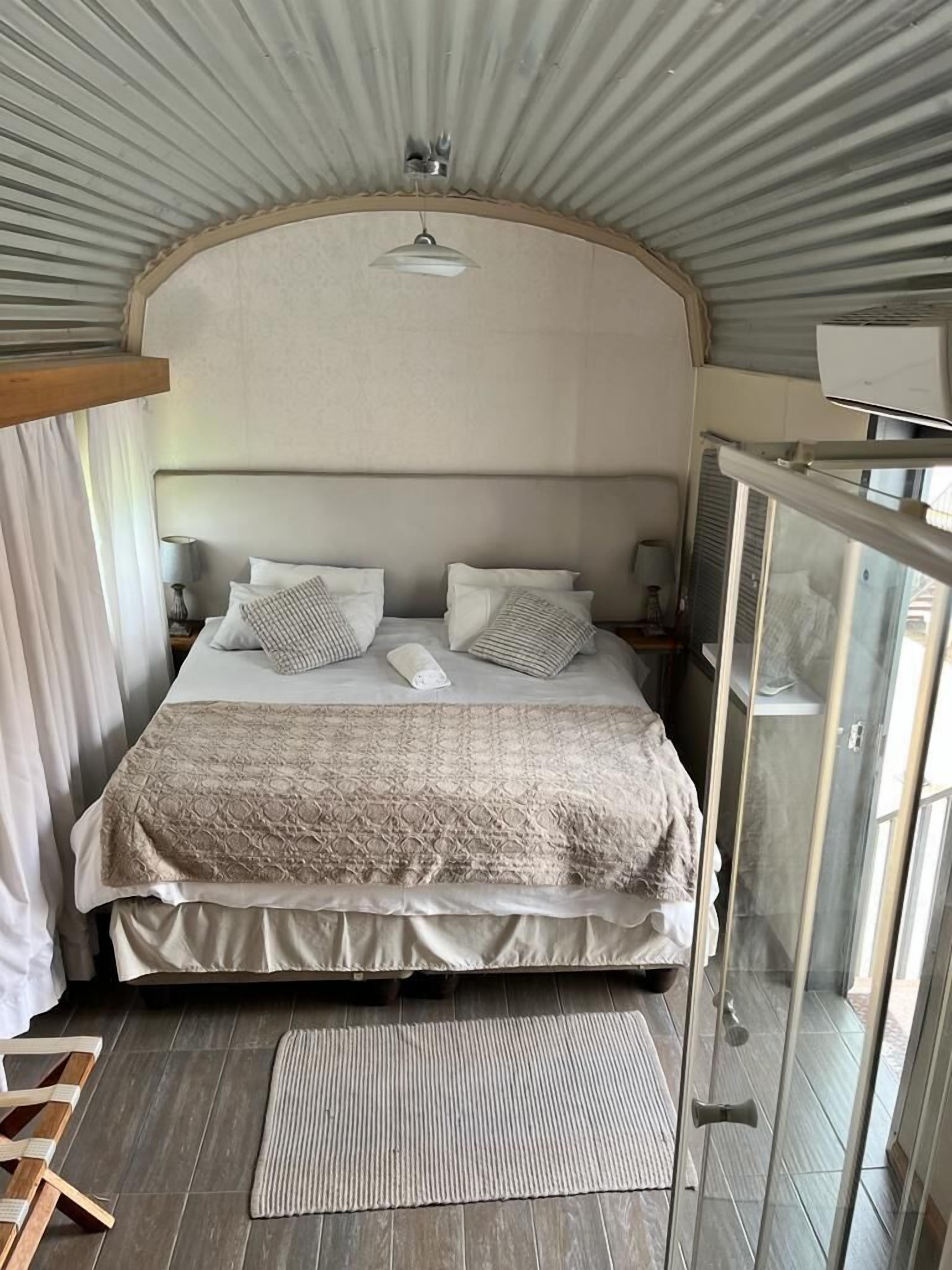 Una camera da letto con un letto, cuscini, un comodino, una lampada e una finestra.