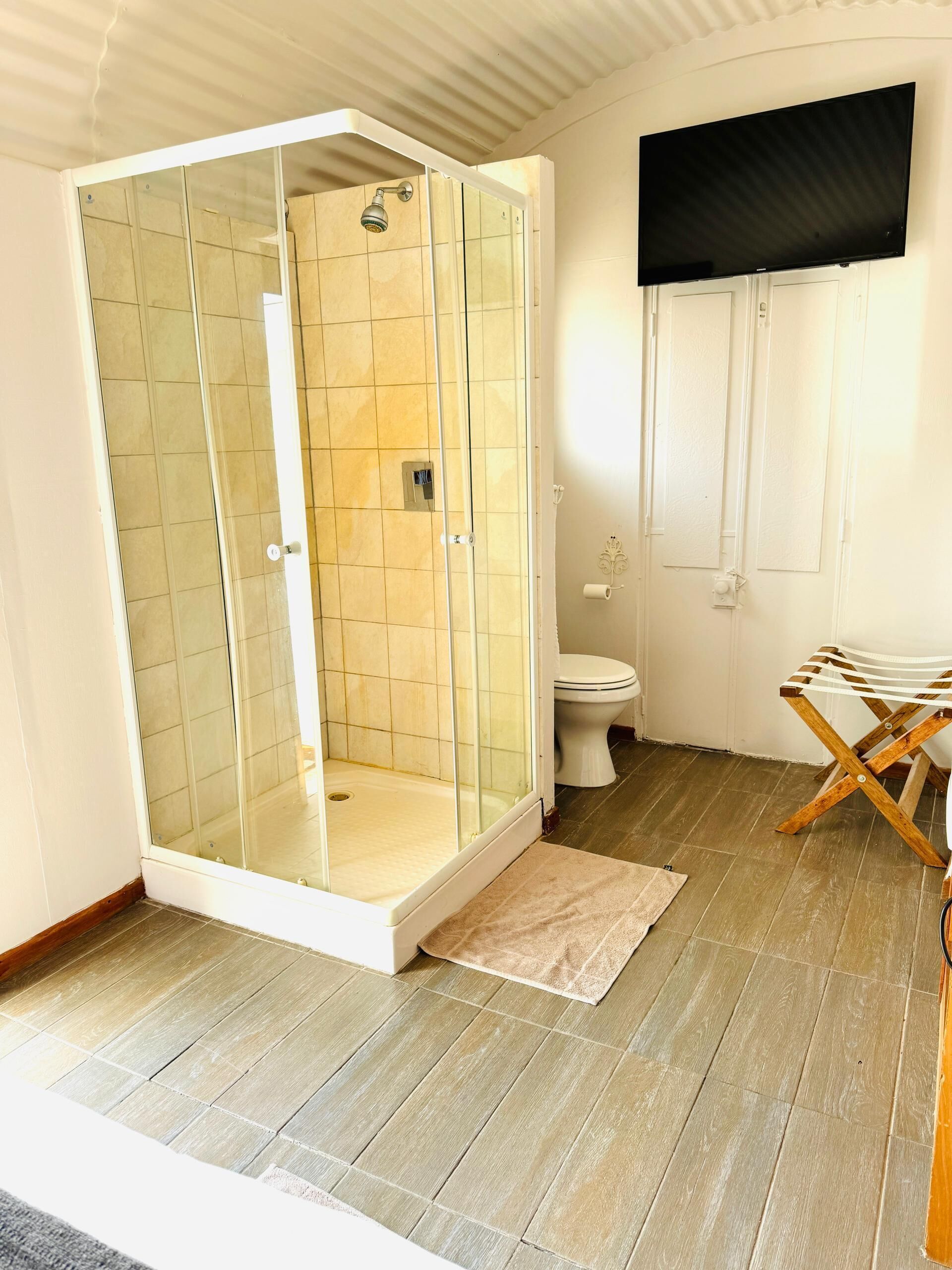 Un baño con ducha de vidrio, inodoro y tendedero de madera.