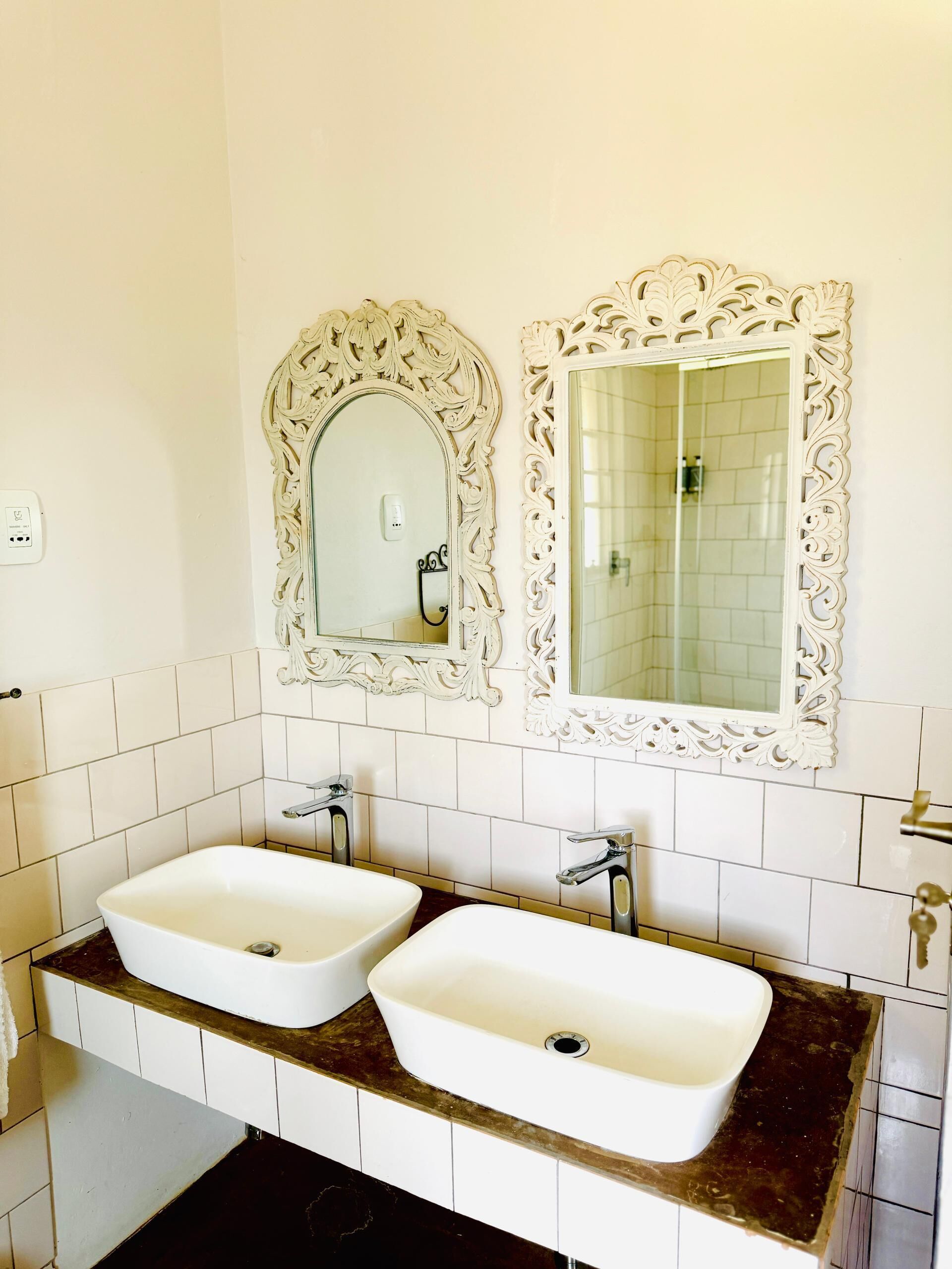 A bathroom with two sinks, ornate mirrors, and a tiled wall.