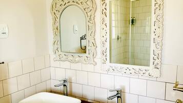 Un baño con dos lavamanos, espejos ornamentados y pared de azulejos.