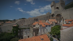 Una muralla de piedra histórica con una torre, tejados de tejas rojas y vistas de los edificios circundantes.