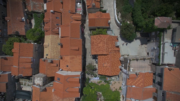 Vista aérea de una zona urbana densamente poblada con tejados de tejas rojas, calles estrechas y algo de vegetación.