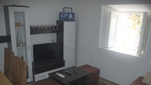 Una sala de estar con televisor, un aparador con cristalería, un sofá y un ventanal.