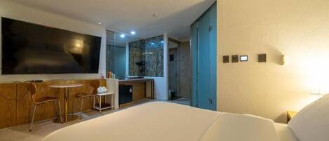 Una habitación de hotel moderna con una cama grande, un escritorio con silla, una kitchenette pequeña y un televisor.