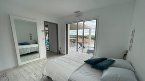 A modern bedroom with a large bed, a sliding glass door leading to an outdoor area, and a view of the sky.