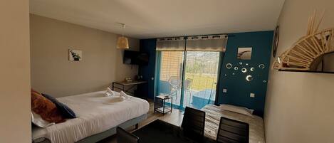 A bedroom with a bed, a desk, a chair, a table, and a balcony with a view.