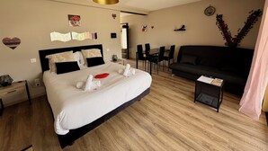Hotellihuone, jossa on sänky, musta sohva, ruokapöytä tuoleineen ja pieni sivupöytä.