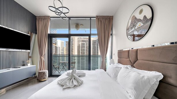 A modern hotel room with a large bed, a flat-screen TV, a balcony with a view of the city, and a large painting on the wall. - Dubai 1BR | Merano Canal View Retreat Near Metro Dining Shops Leisure (Business Bay)
