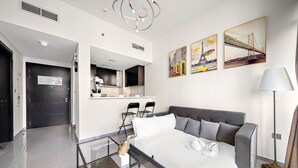 A modern hotel room with a bed, a glass coffee table, a sofa, and a dining area with chairs. There are paintings on the wall and a lamp next to the sofa. - Dubai 1BR | Merano Canal View Retreat Near Metro Dining Shops Leisure (Business Bay)