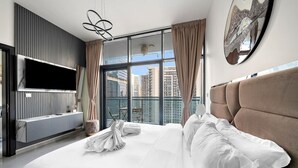 A modern hotel room with a large bed, a flat-screen TV mounted on the wall, and a city view through the large window. - Dubai 1BR | Merano Canal View Retreat Near Metro Dining Shops Leisure (Business Bay)