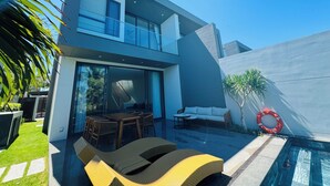 A modern two-story house with a glass facade, outdoor seating area, and a swimming pool.
