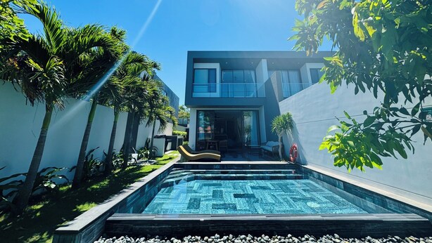 A modern house with a swimming pool, surrounded by palm trees and greenery.