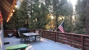 A wooden deck with a picnic table and chairs, surrounded by trees and a red railing. - Rustic Sierra Cabin with Hiking Trail and Kids Room - Perfect Family Getaway! (Mi-Wuk Village)