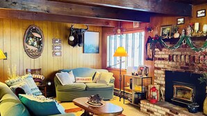 A cozy living room with a fireplace, wooden walls, a sofa, and a coffee table. - Rustic Sierra Cabin with Hiking Trail and Kids Room - Perfect Family Getaway! (Mi-Wuk Village)