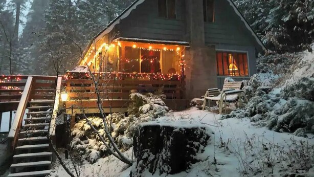 A cabin with a wooden staircase leading to a porch, surrounded by snow-covered ground and trees. - Rustic Sierra Cabin with Hiking Trail and Kids Room - Perfect Family Getaway! (Mi-Wuk Village)
