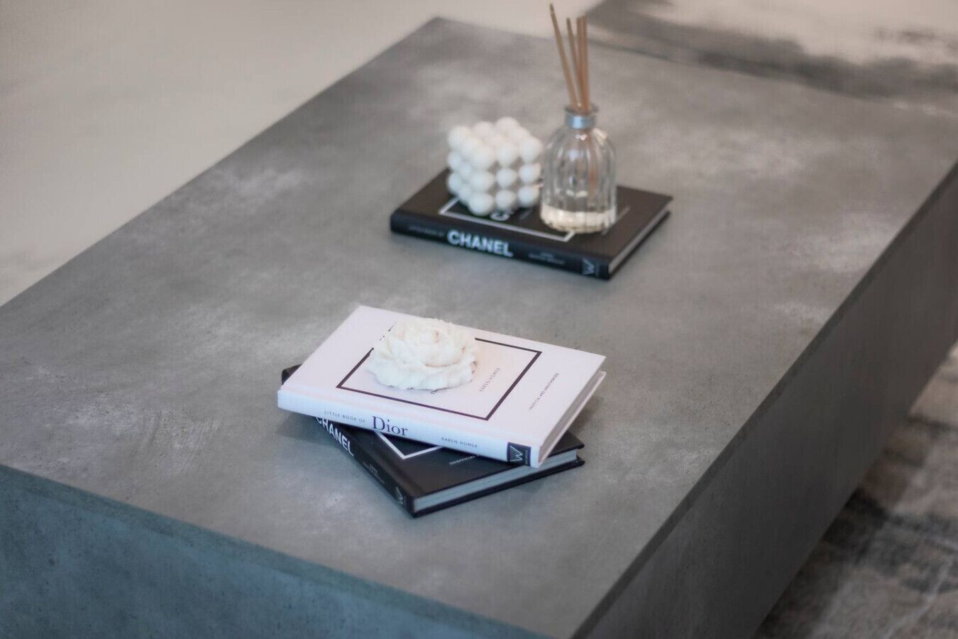 A modern, minimalist table with a book titled "Dior" and a small decorative item with a candle and reed diffuser.