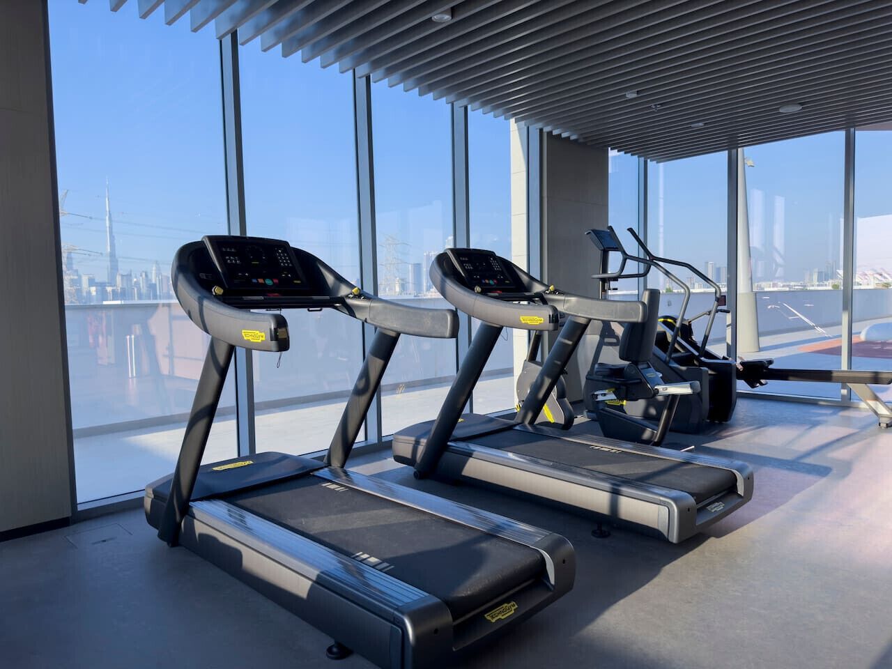 A gym with treadmills and exercise equipment, large windows with a city view.
