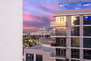 A modern multi-story building with balconies and large windows, overlooking a cityscape with a sunset sky.