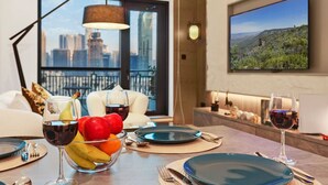 Une chambre d’hôtel moderne dotée d’un coin repas, d’une grande fenêtre offrant une vue sur la ville, d’un téléviseur fixé au mur et d’un balcon avec vue panoramique sur la ville.