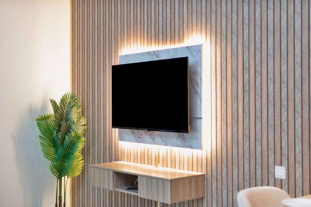 Un salon moderne avec un téléviseur à écran plat fixé à un mur en bois orné de lattes verticales, une console en bois en dessous et une plante en pot sur la gauche.