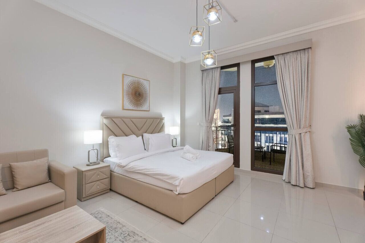 Quarto moderno com cama grande, mesas de cabeceira, sofá e varanda com cortinas.
