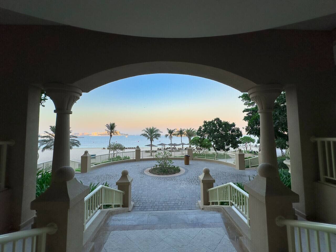 Une vue depuis un balcon donnant sur une plage bordée de palmiers, sous un ciel dégagé.