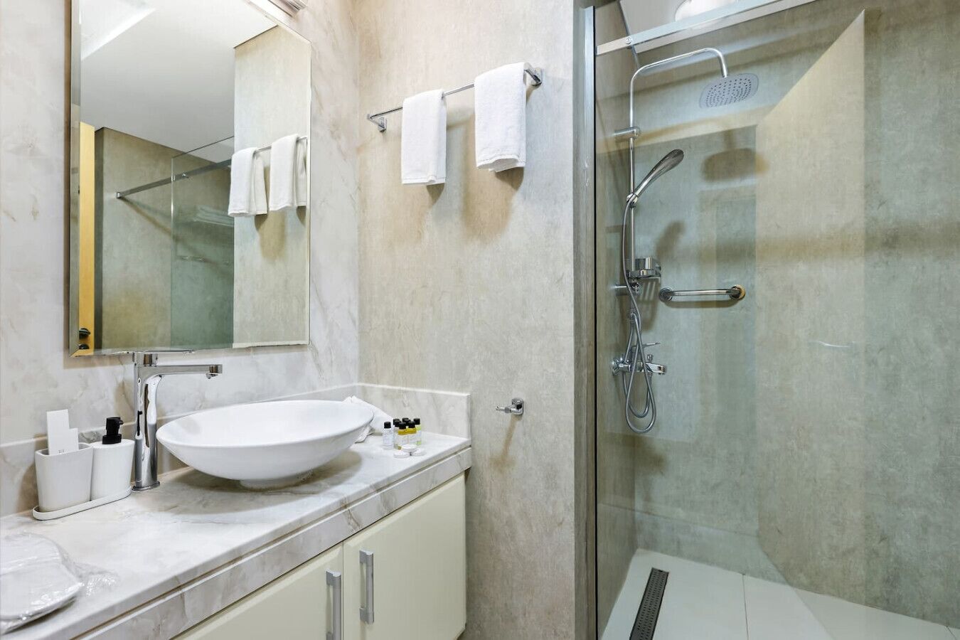 A modern bathroom with a large white sink, a glass shower enclosure, and a marble countertop.