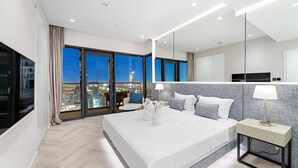 Quarto de hotel moderno com uma cama grande, mesa de cabeceira, espelho e vista para a cidade.