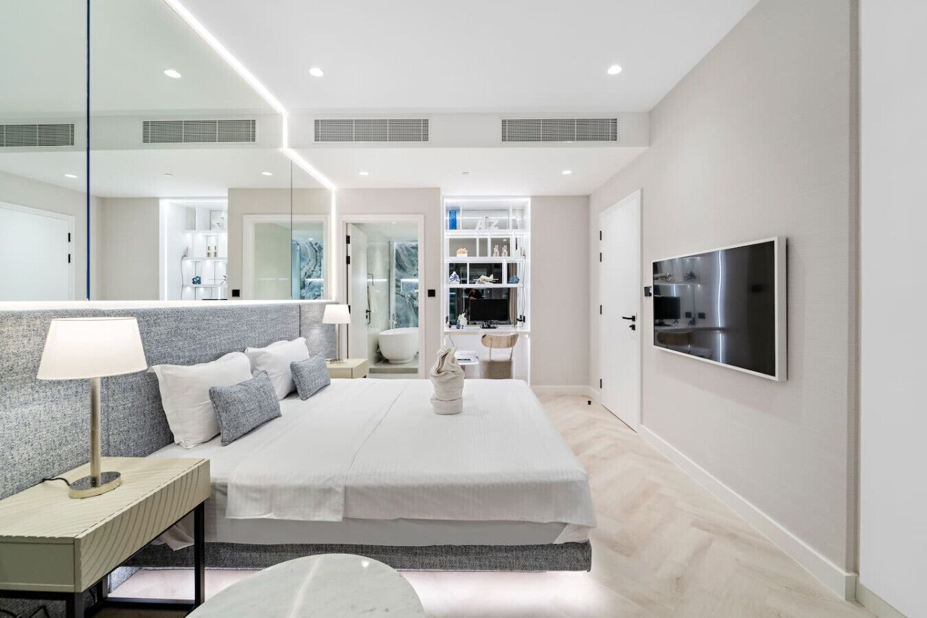 A modern bedroom with a large bed, bedside table, lamp, and a TV mounted on the wall.