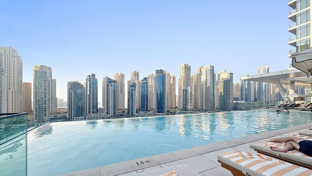 A rooftop pool with a city skyline view, lounge chairs, and a clear sky. - First-Class Marina Stay with Views, Gym, and Free Parking (Dubai)