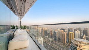 Varanda de um edifício alto com vista para a cidade, assentos modernos e guarda-corpo de vidro.