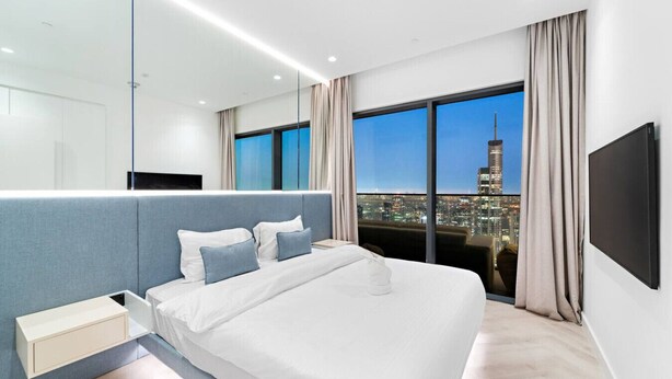 Quarto de hotel moderno com cama grande, mesa de cabeceira, televisão fixada na parede e vista para a cidade.