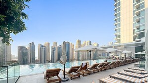 Uma área de piscina no terraço com espreguiçadeiras e guarda-sóis, com vista para o horizonte da cidade.