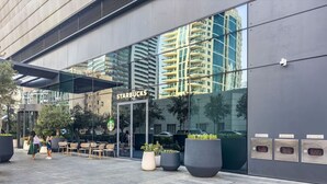 Um Starbucks com área externa, grandes vasos de plantas e fachada de prédio moderna.