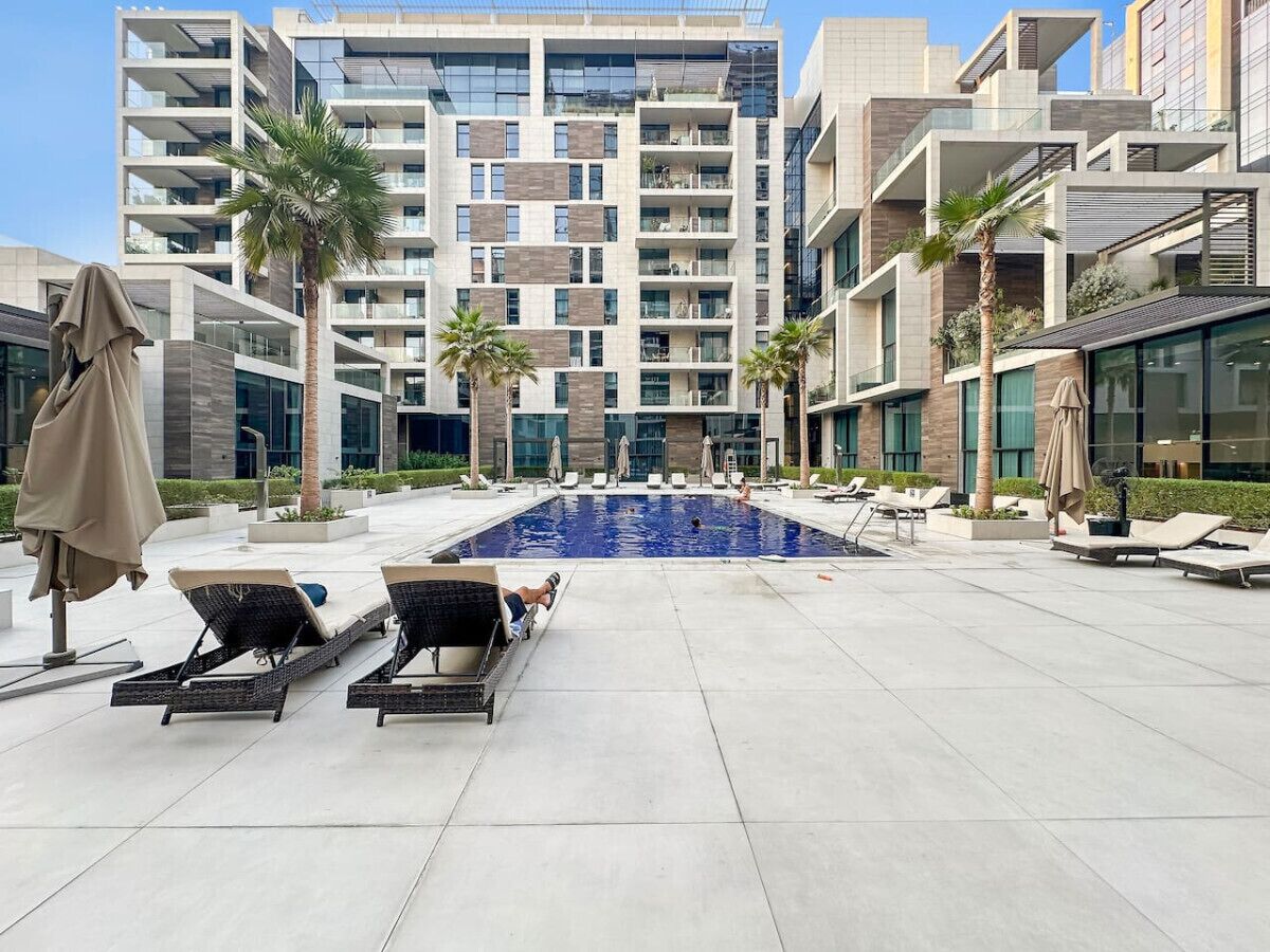 A modern hotel with a rooftop pool, lounge chairs, and palm trees.