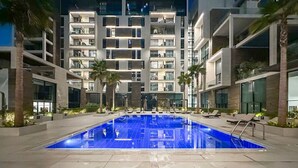 Ein Swimmingpool mit Liegestühlen und Palmen, umgeben von modernen Gebäuden.