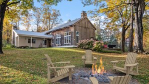 Eine rustikale Holzhütte mit Feuerstelle und Adirondack-Stühlen inmitten von Bäumen.