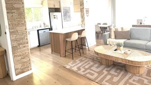 Ein modernes Wohnzimmer mit rundem Couchtisch, einem grauen Sofa und einem durch einen offenen Durchgang sichtbaren Küchenbereich.