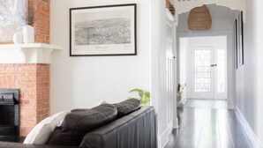 Una sala de estar moderna con piso de madera oscura, un sofá de cuero negro, una chimenea y un pasillo que lleva a una puerta.